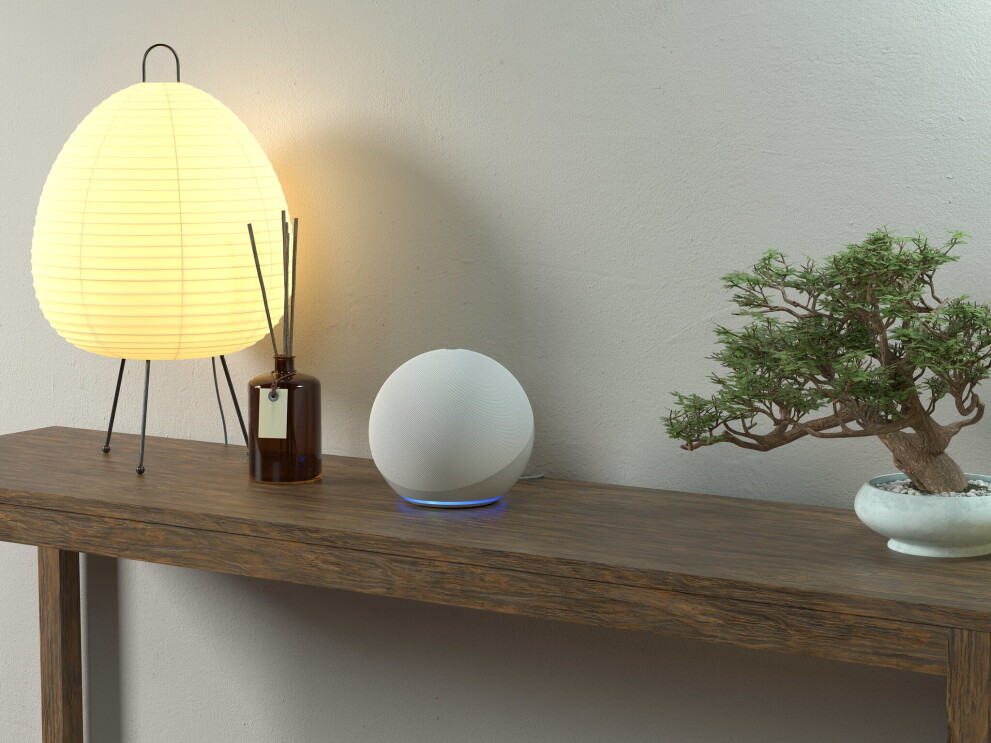 Echo Dot on a table next to a lamp, a reed diffuser and a bonsai tree. 