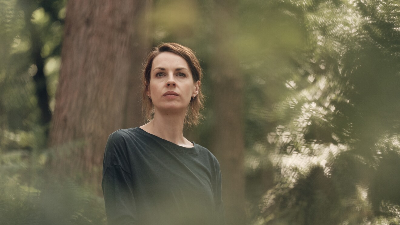 A brunette woman looks pensively in a forest