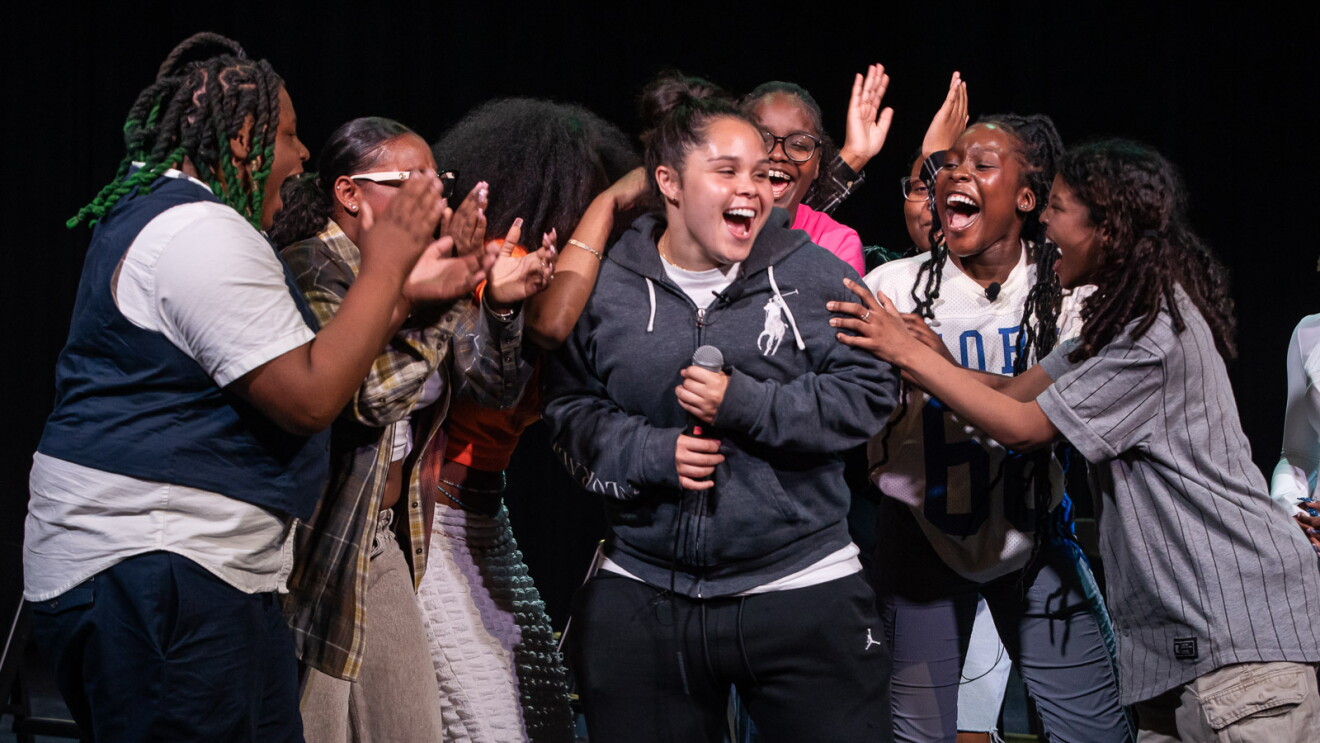 Enthusiastic youth gathering with central performer singing as friends clap and cheer