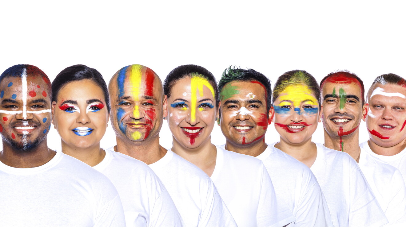 Para el Día de la diversida Amazon ha preparado una acción con asociados de diferentes países que llevan la bandera pitnada en su cara. En la foto, con camiseta blanca 8 trabajadores de Amazon con una camiseta blanca y mirando sonriendo a cámara.  Ángel, Ingrid, Adrián, Giselle, Ricardo, Gladys, Mohamed y David. 