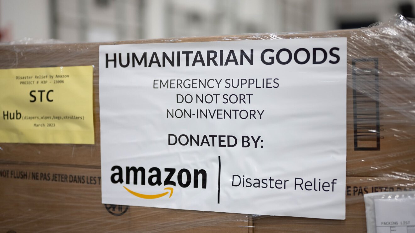 An image of a box with a white sign on it that says "Humanitarian Goods Emergency Supplies Do Not Sort Non-Inventory Donated by Amazon | Disaster Relief"