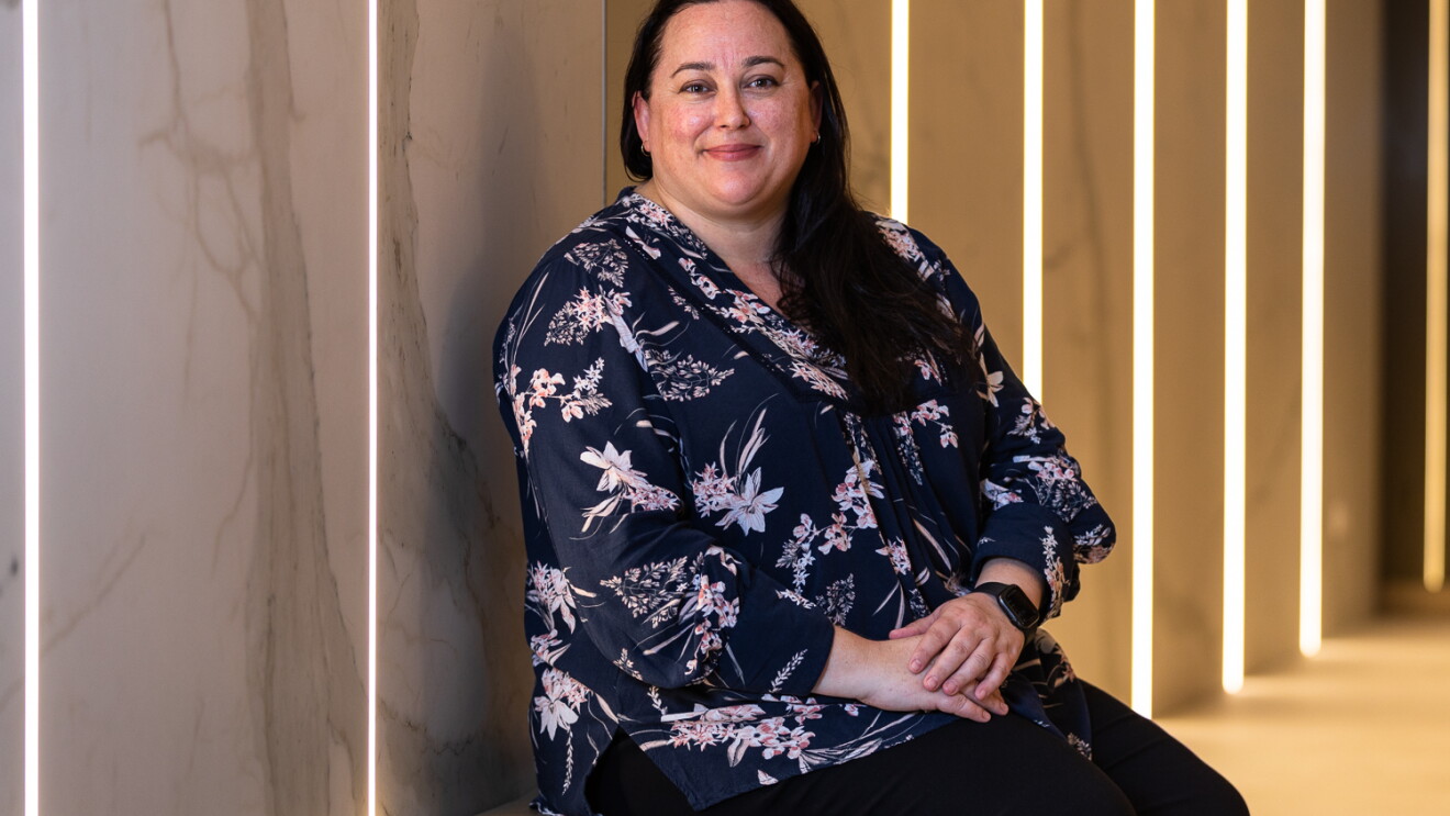 An image of a woman sitting on a bench in a hallway while smiling for a photo. 