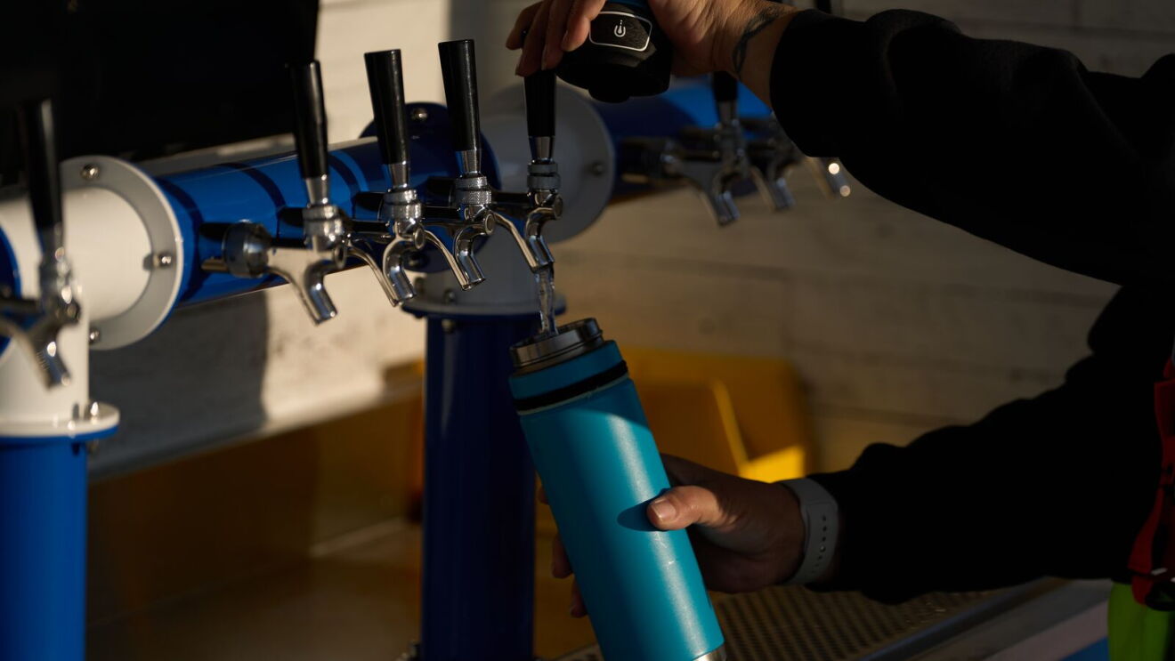 Person filling reusable water bottle from tap system with multiple chrome dispensers