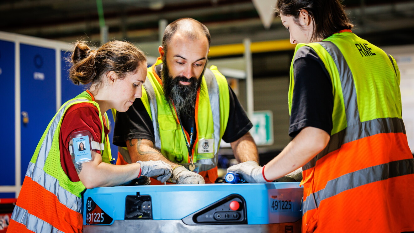 Tre trabajadores de un centro logístico de Amazon arreglando un robot. 