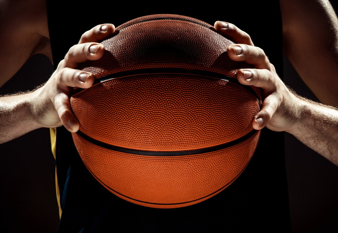 Silhueta vista de jogador de basquete segurando bola de basquete na parede preta