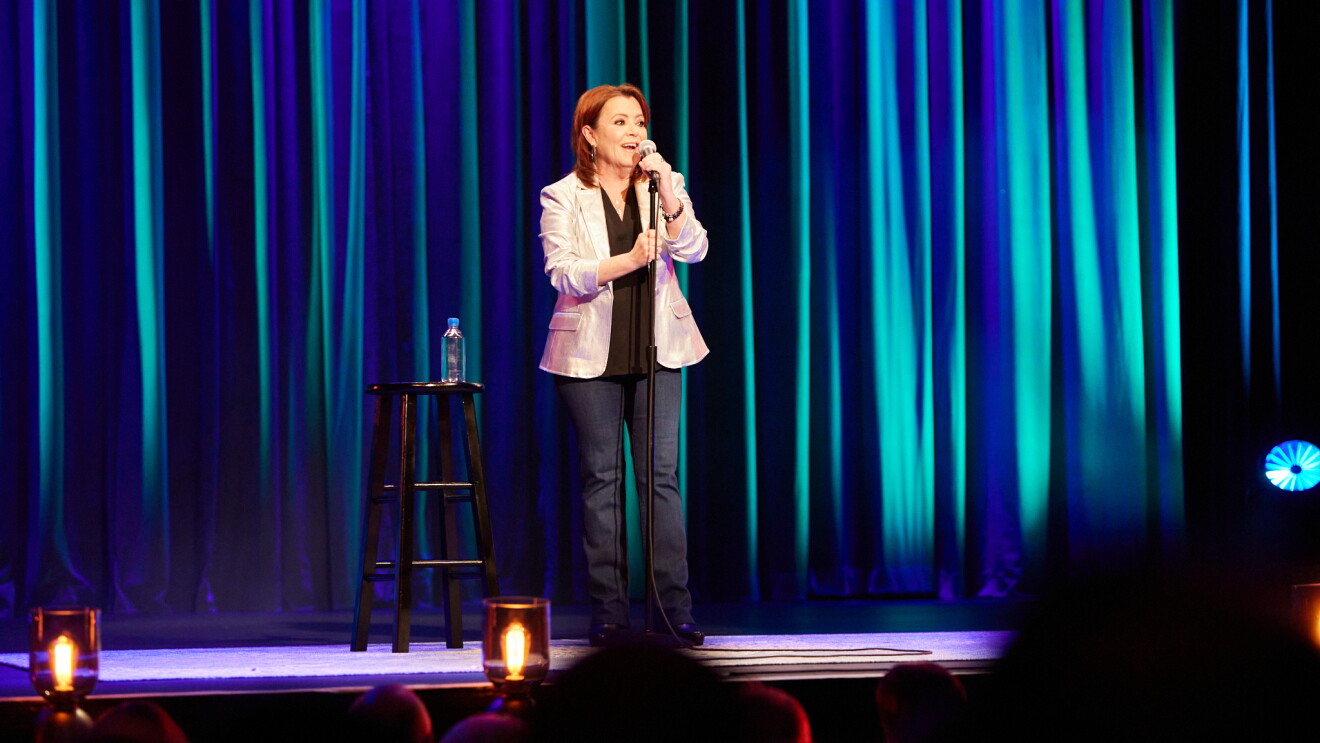 Kathleen Madigan performing on stage with blue curtain backdrop