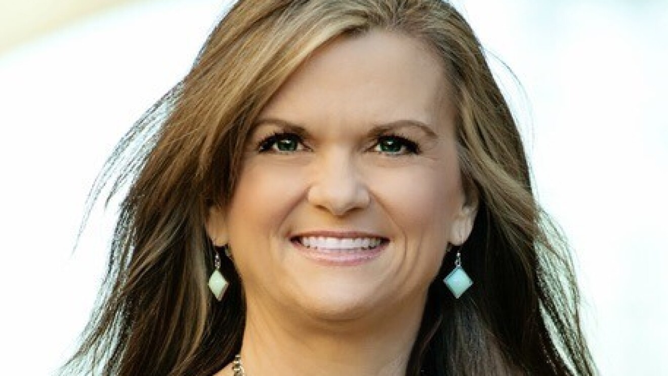 儿童读物作家帕姆·卡尔弗特的肖像。她穿着一件背带皮夹克,戴着一条浅绿色的项链,上面有小玩意。她对着镜头微笑。