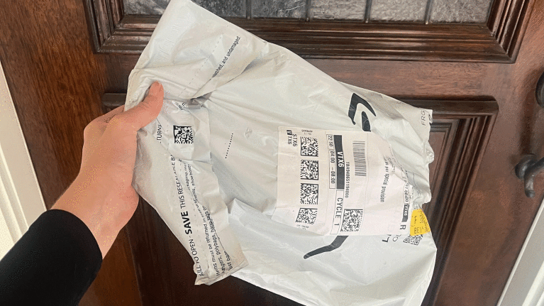 An image of a hand holding an Amazon package outside of a doorstep.