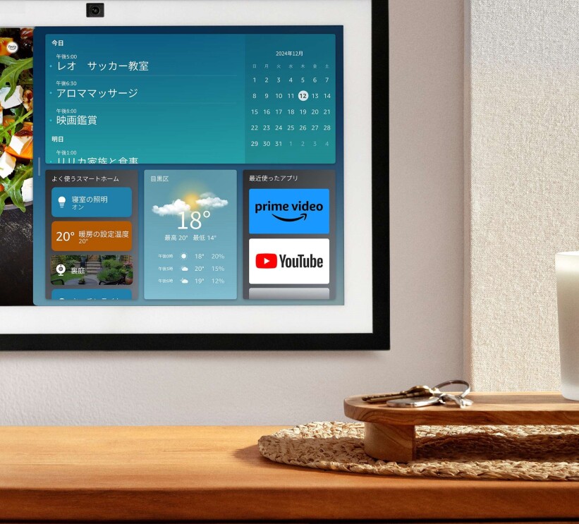 壁に掛けられているEcho show 15の画面にスケジュールや天気予報が表示されている。そのタブレットの手前には鍵とキャンドルが木材で作られたカウンターに置かれている。