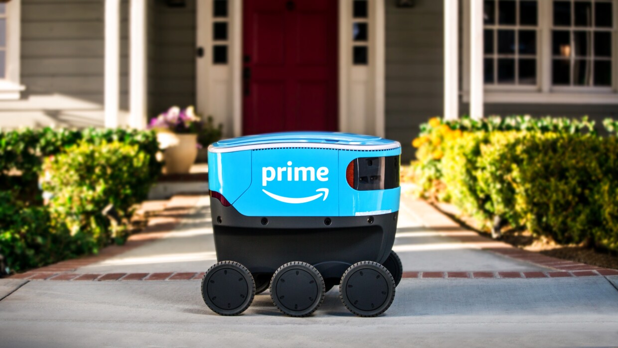 A small blue delivery bot with Amazon Prime branding sits on a walkway that leads to a house.