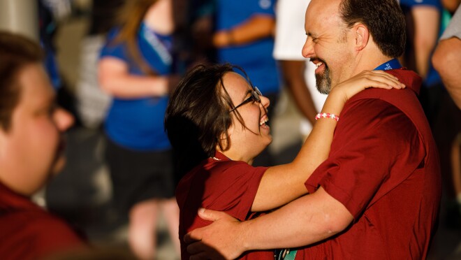 两个美国特奥会运动员(男性和女性,在红衫军)舞蹈在前台,志愿者站在后台。