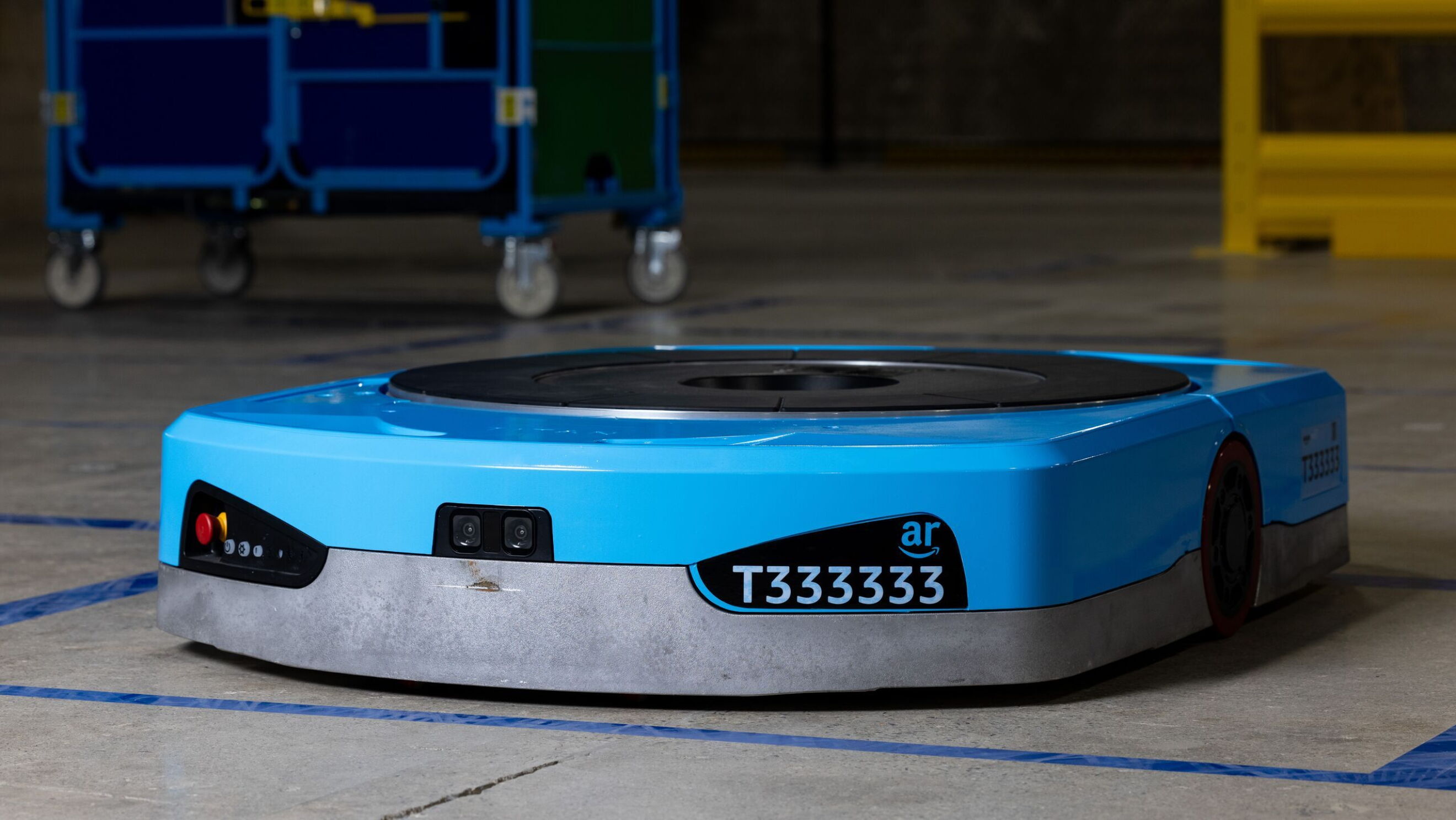 An image of Amazon's new Titan robot. It's blue, plate-like robot with black details, including a camera on the front, a name plate that says "T333333" and a large, circular plate on top.