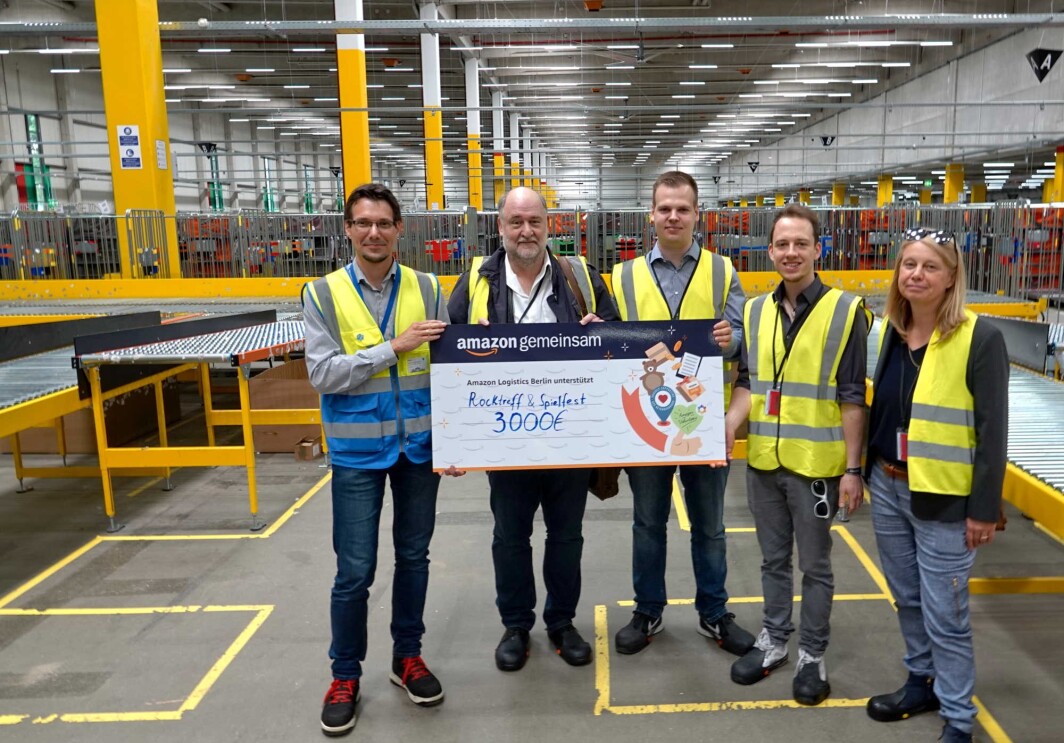 Fünf Personen stehen im Verteilzentrum bei Amazon und halten einen Spendenscheck
