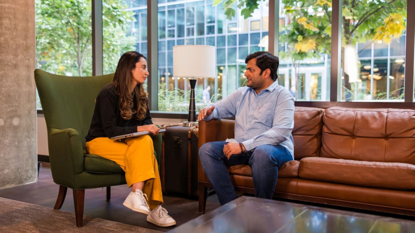 Professional conversation between woman in yellow pants and man on leather couch