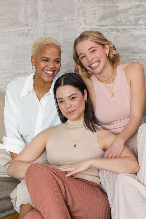 Drei Frauen sitzen auf einem Sofa und lachen in die Kamera.