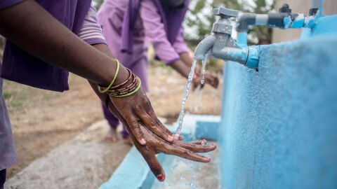 两个人在室外水龙头边洗手的照片。