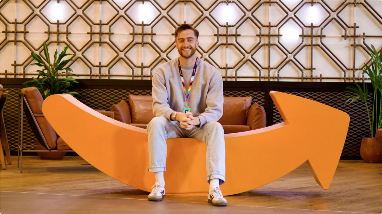 Smiling man dressed casually sitting on giant Amazon Smile logo