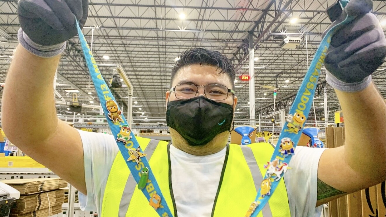 A man, an employee at an Amazon fulfillment center, holds up a lanyard with many pins on it.