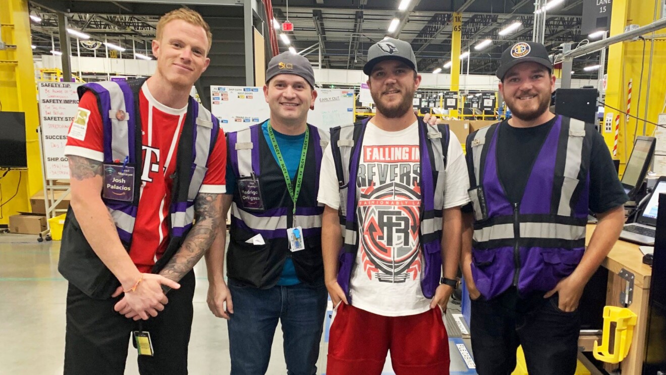 Josh smiles for a picture standing next to his colleagues in an Amazon fulfillment center.