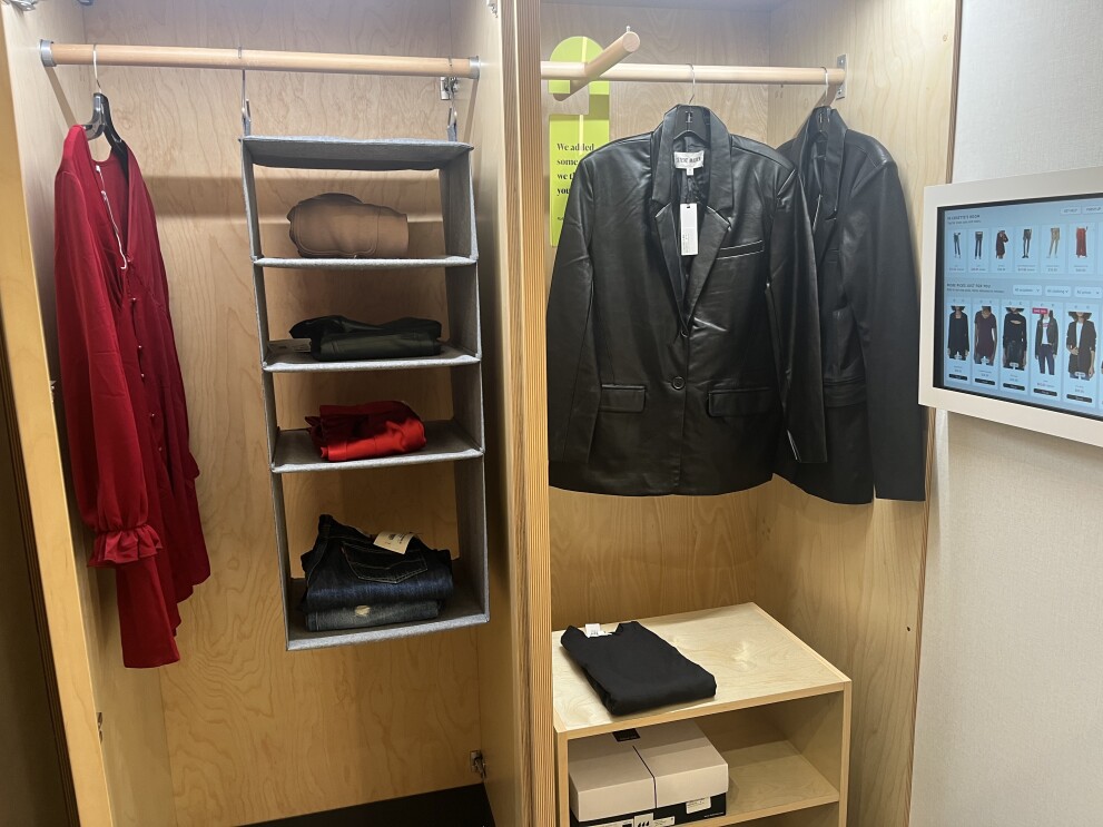 An image of a closet inside a fitting room. There are several items hung up and folded on the shelves and racks.