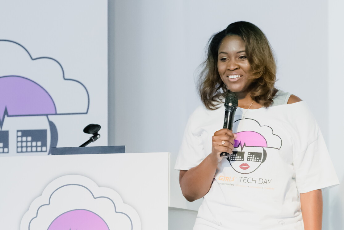 Cornelia Robinson, Global Leader of AWS InCommunity holding a microphone and wearing a Girls' Tech Day T-shirt speaks at an AWS InCommunity event