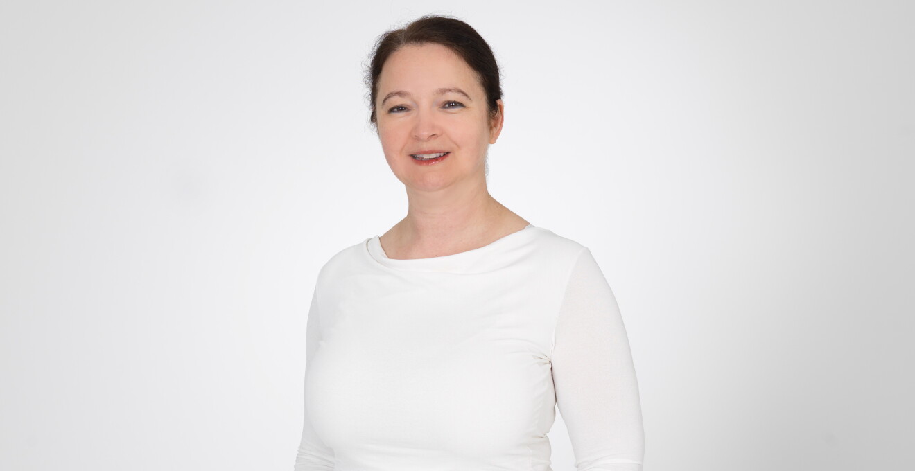 AWS Mitarbeiterin Agnes Balazs mit weißem Oberteil vor einer weißen Wand stehend.