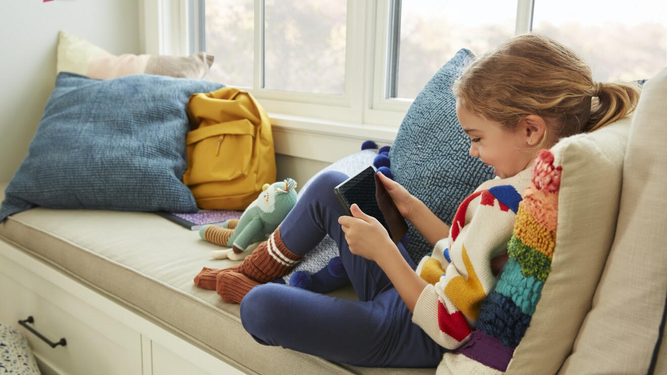 Smiling child sitting in a window nook using a Fire tablet
