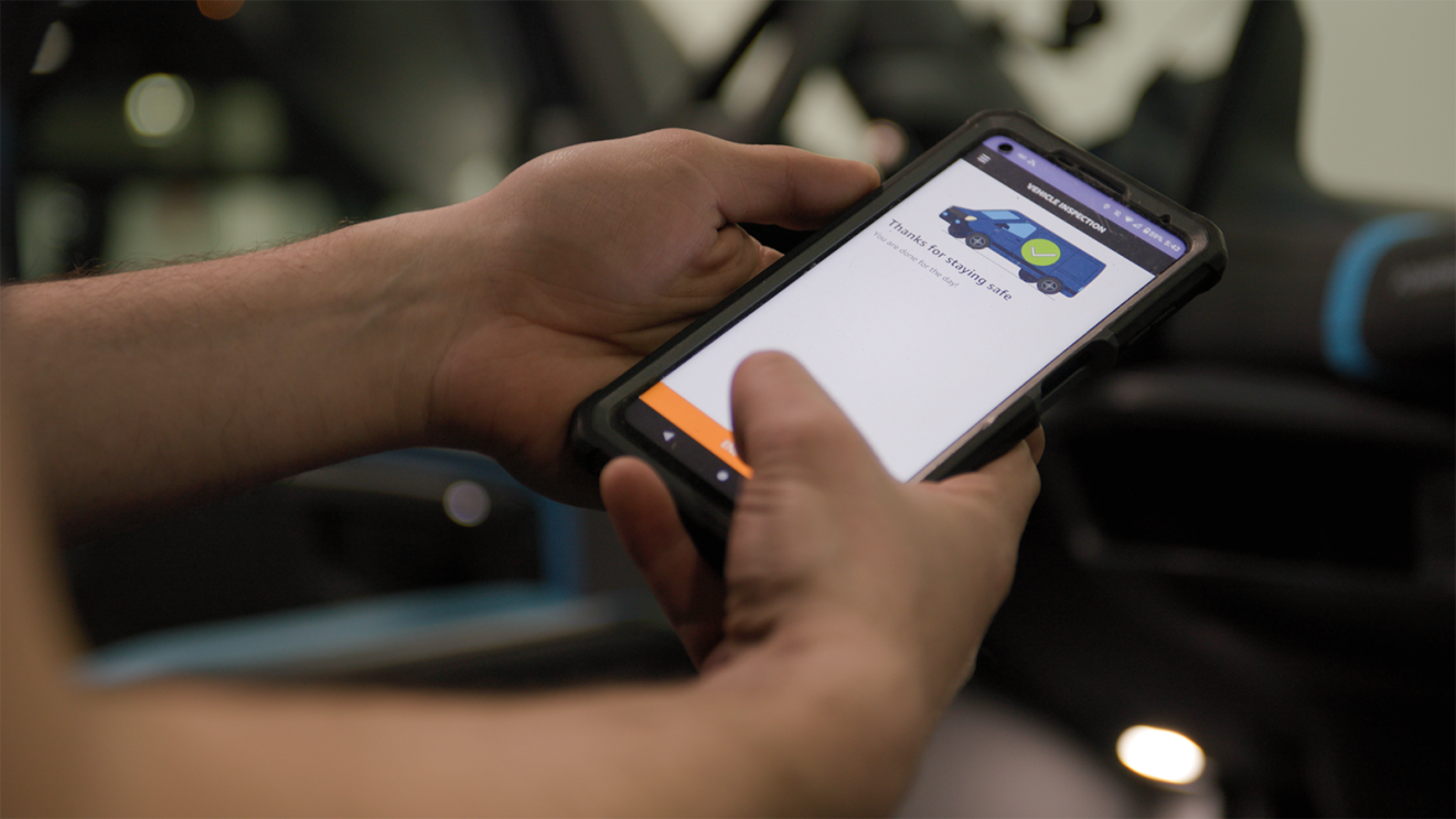 An Amazon delivery driver holds a phone with a safety check on the screen.
