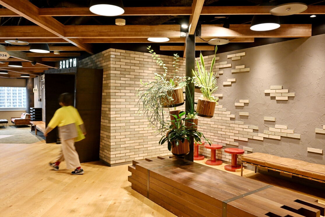 部屋の中央に縦型の植物と木製のベンチが置かれている。その部屋にはレンガの壁が半分タイル張っている。
