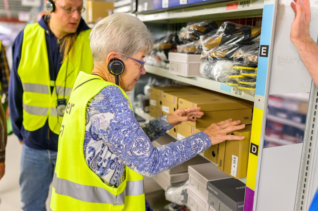 Eine Besucherin steht vor einem Regal im Logistikzentrum und ertastet die Artikel.