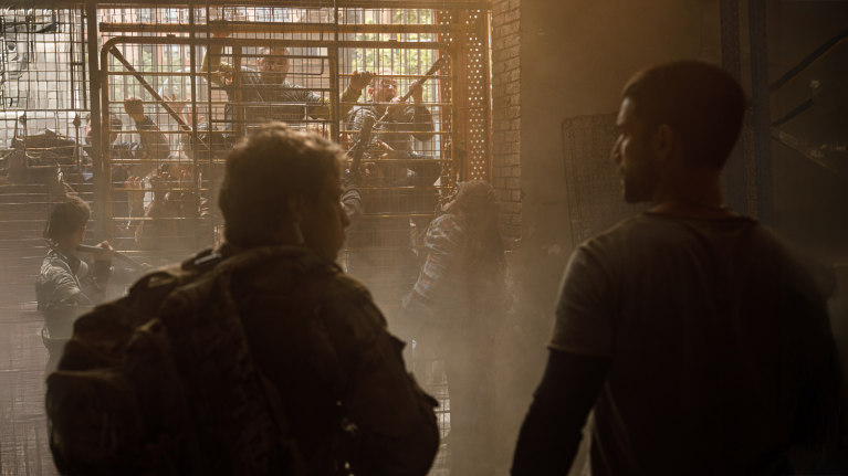 the backs of two men who face the a fence where people are trying to climb in