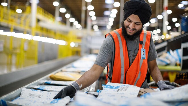 在华盛顿州肯特BFI5的亚马逊物流中心,一名亚马逊员工穿着安全手套和背心,处理客户订单。