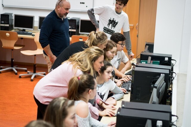 Mädchen und Jungen sitzen vor Computer-Bildschirmen. Sie schauen alle in die Bildschirme.