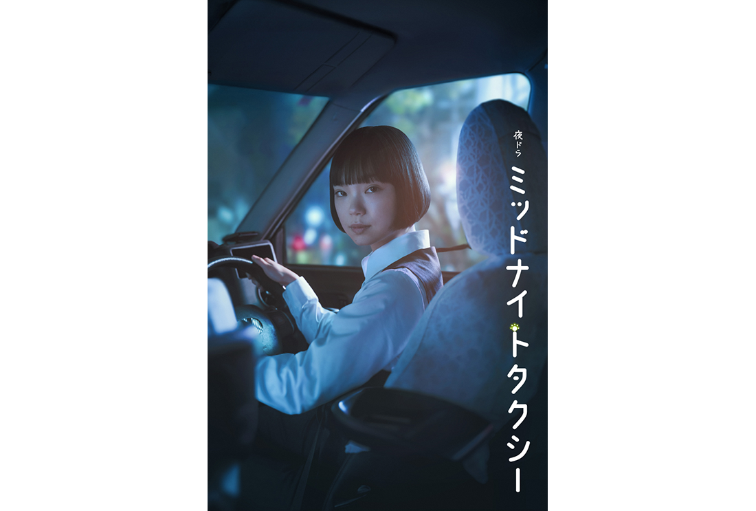 タクシーの車内、運転席に座った女性運転手が肩越しに振り向き、後部座席を見つめている。