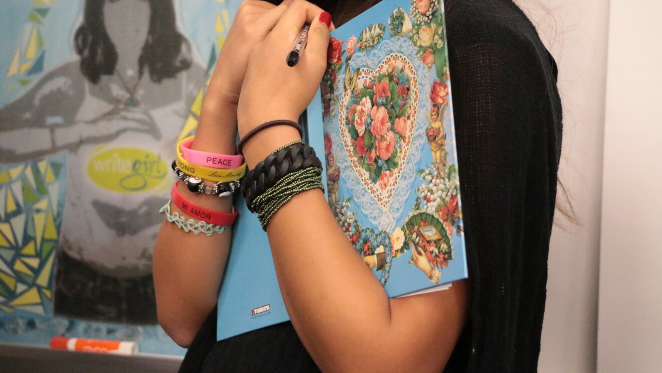 An image of arms holding an open book. The person is wearing a variety of bracelets showing their personality. 