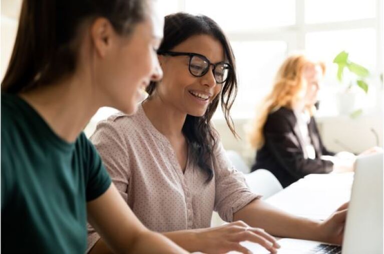 zwei junge Frauen sitzen vor dem Computer und besprechen sich