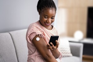 An image of a woman using a patch on her arm and looking at her phone. 