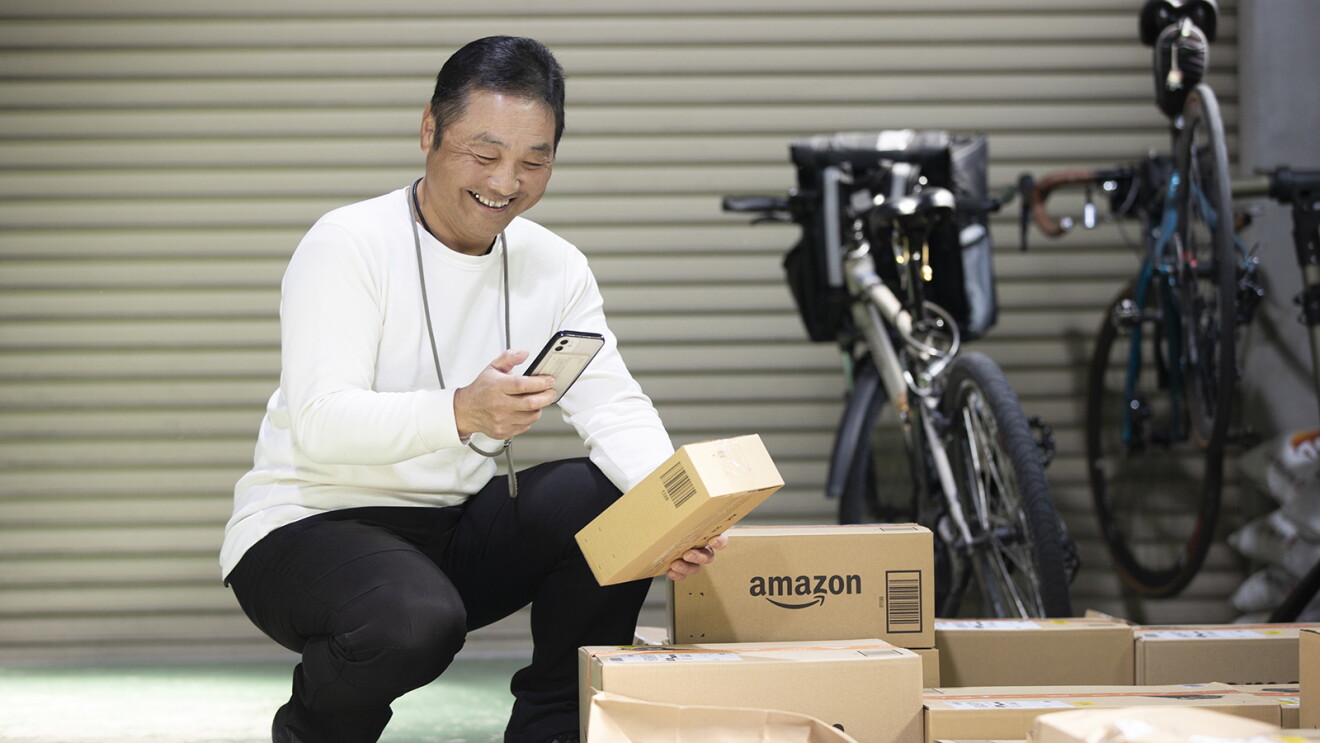 自転車の前でAmazonの段ボールにスマートフォンを向けている男性