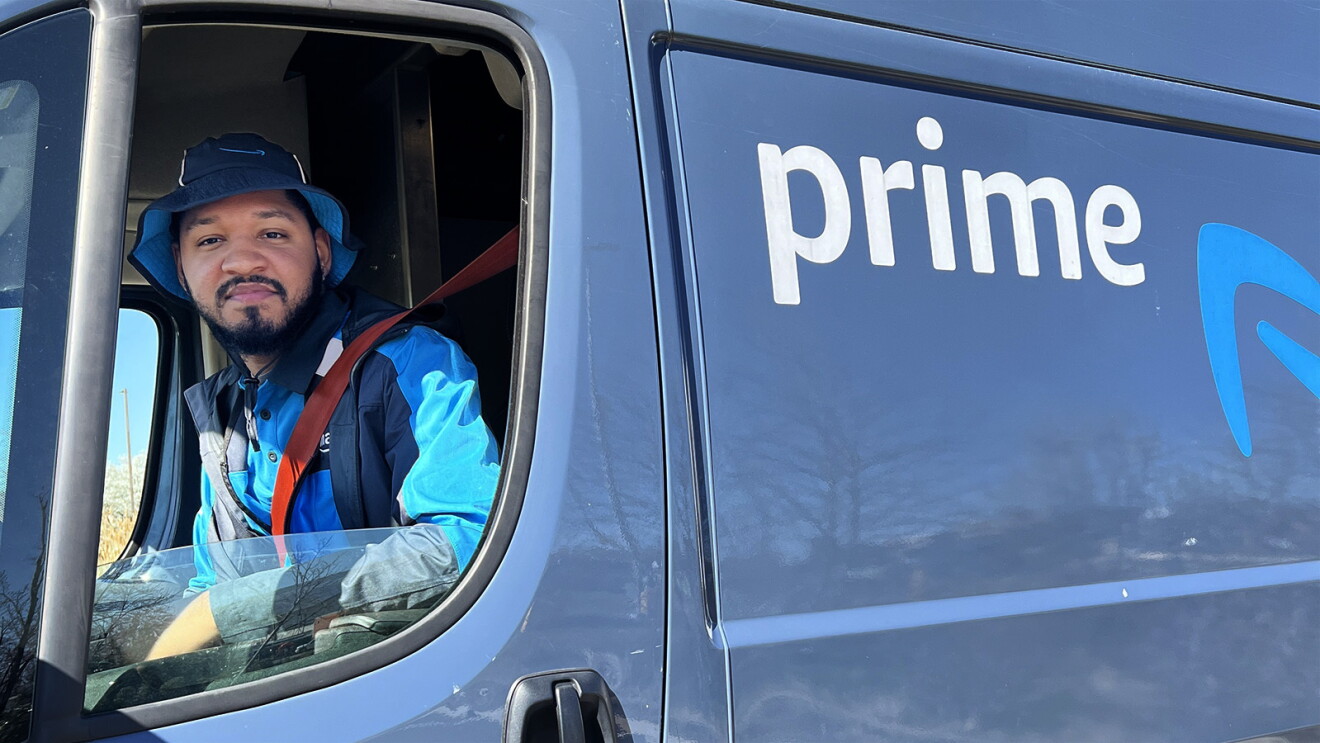 Torazz Richardson an Amazon delivery driver sits in the driver seat of a delivery vehicle with his window rolled down.