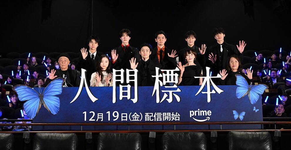 「人間標本」の大きな文字が配置された青いパネル、その後ろに10人の人物が2列に並んで手を振っている。後方の観客は青いペンライトを振る。