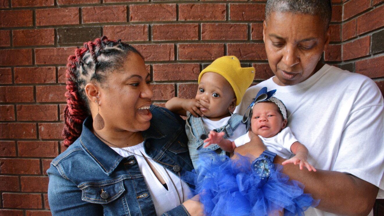 Two people hold their infants together on the front step of their home. 