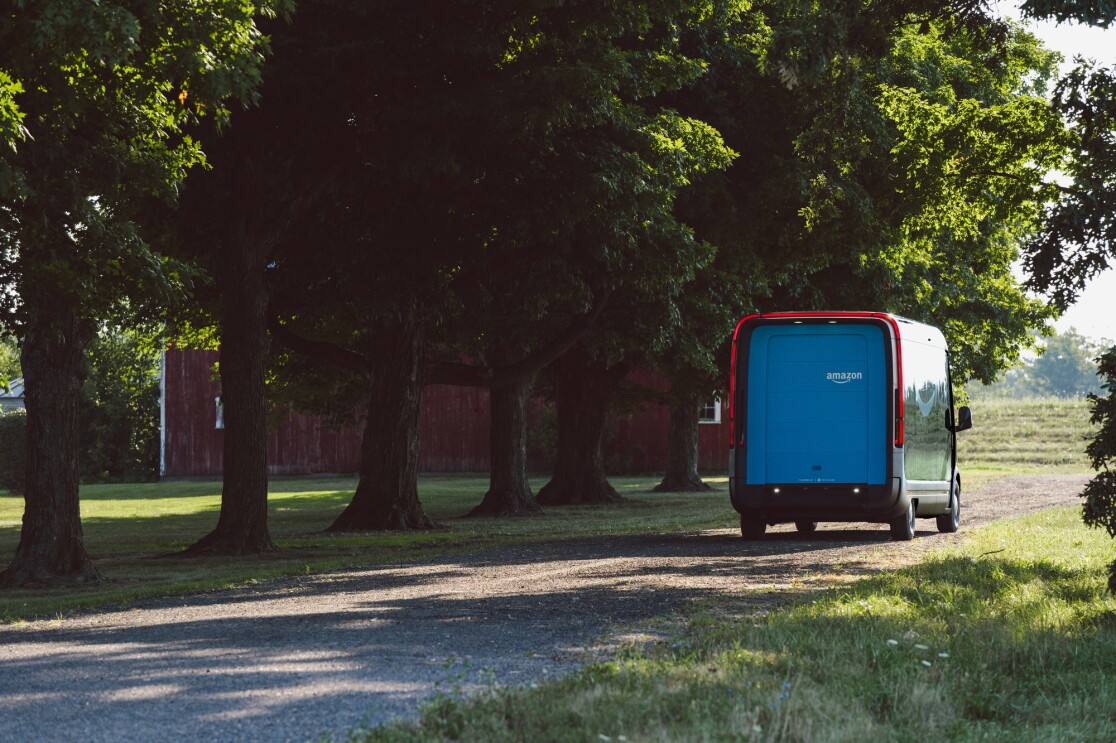 An electric delivery vehicle seen from behind, driving along a wooded road.