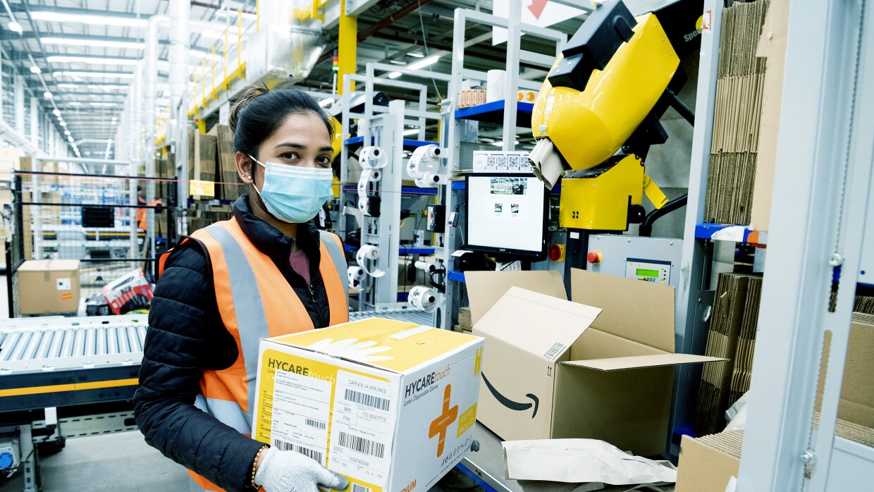 An Amazon fulfilment centre employee packing boxes with medical supplies in the Coalville Fulfilment centre to provide supplies to the relevant government centres. She is wearing protective gloves and a face mask.