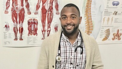 亚马逊的伤害预防专家沙奎尔·罗宾逊(Shaquille Robinson)站在一面墙前,墙上贴着人类肌肉解剖结构的海报。他看着摄像机,脖子上戴着听诊器。