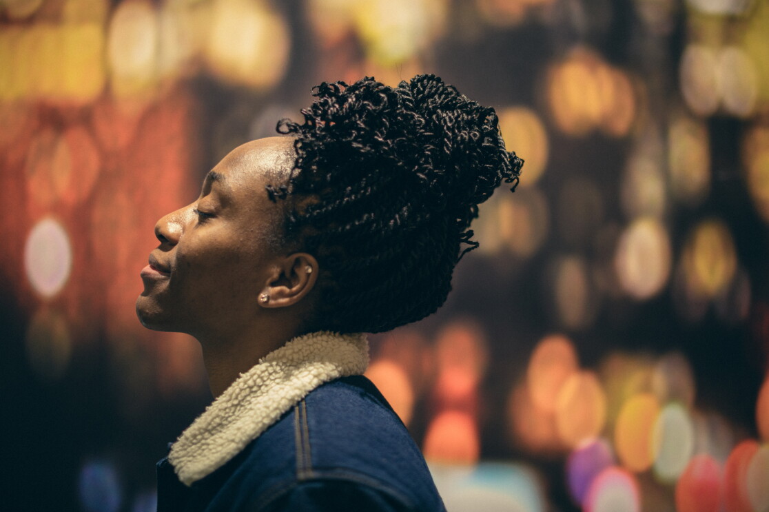 A woman in a blue jacket is photographed in profile. Her eyes are peacefully closed and she is looking skyward. 
