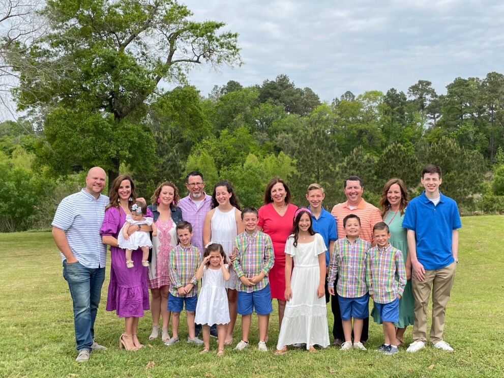 Rebecca is surrounded by her children and grandchildren outside as they all pose and smile for a family photo.