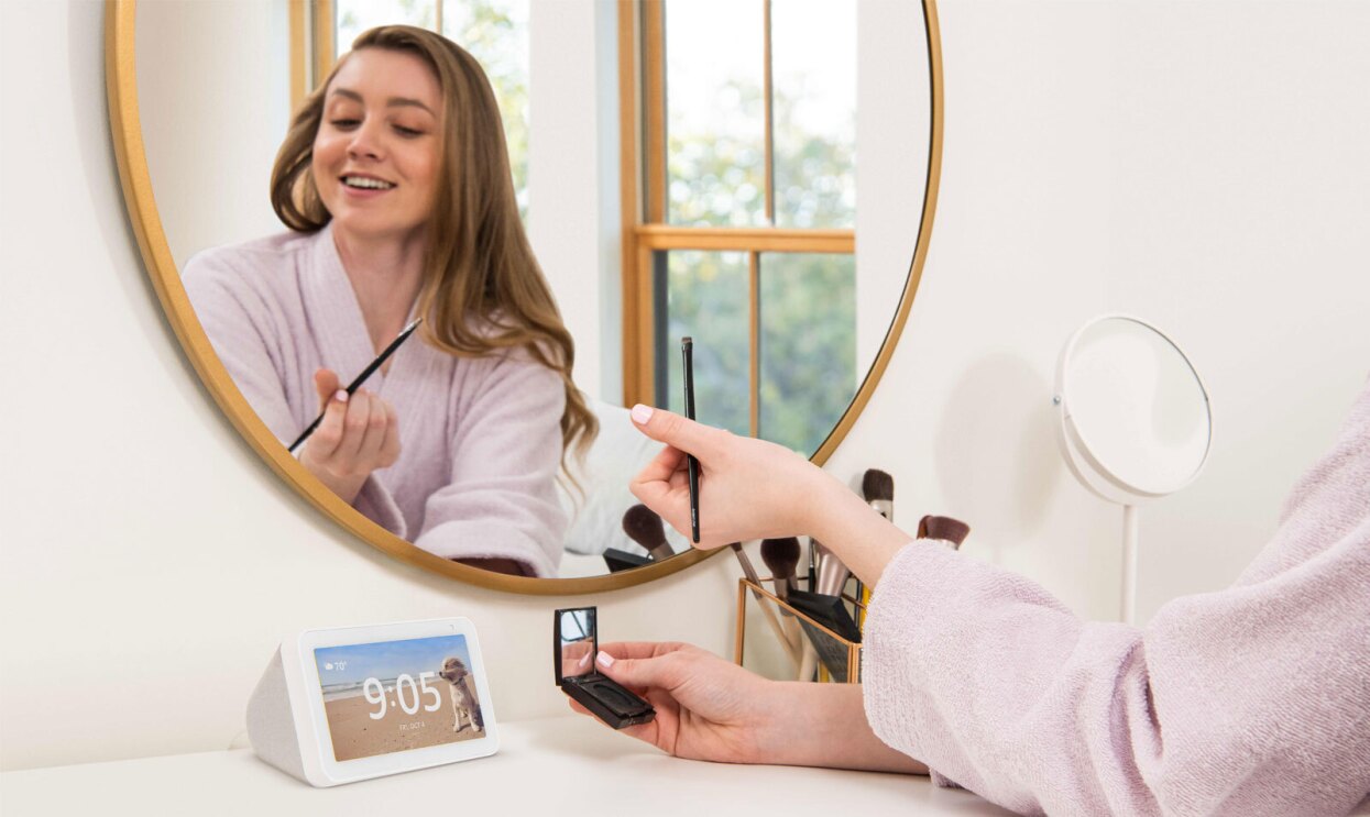 An image of a woman putting on make up and an Echo Show sitting on the vanity table. 