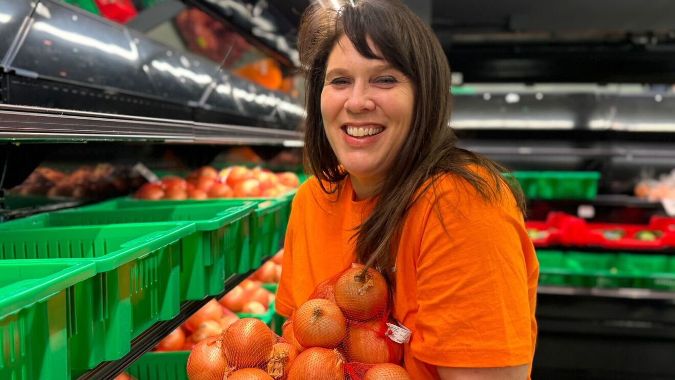 Smiling woman in orange volunteer shirt holding bag of onions in produce section