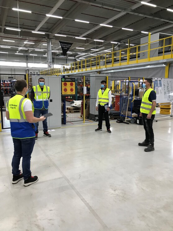 4 Mitarbeiter mit Sicherheitswesten und Masken in einer Logistikhalle