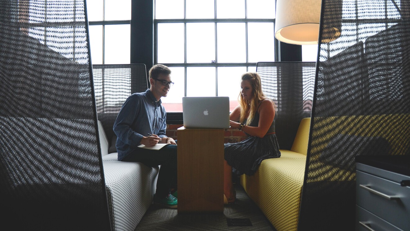 Man taking notes as his female colleague works on a laptop, in a casual work space.